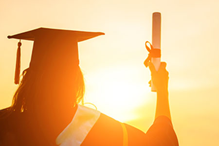 A graduate, with diploma in hand, looks into the sun and her future.