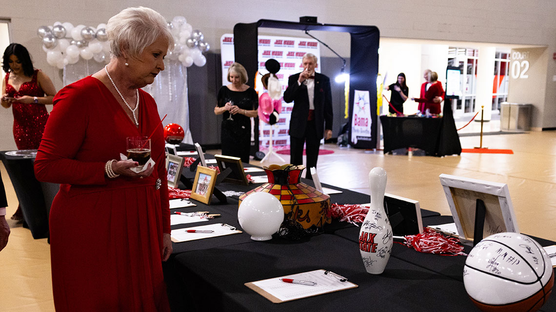 An alumna browses items on a silent auction table at the annual Red Tie Dinner and Auction. In this photo she is looking at a bowling pin signed by the national championship 2023-2024 Jax State Bowling team.