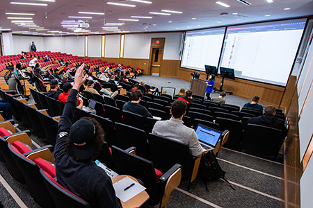 A student raises his hand in a classroom in merrill hall