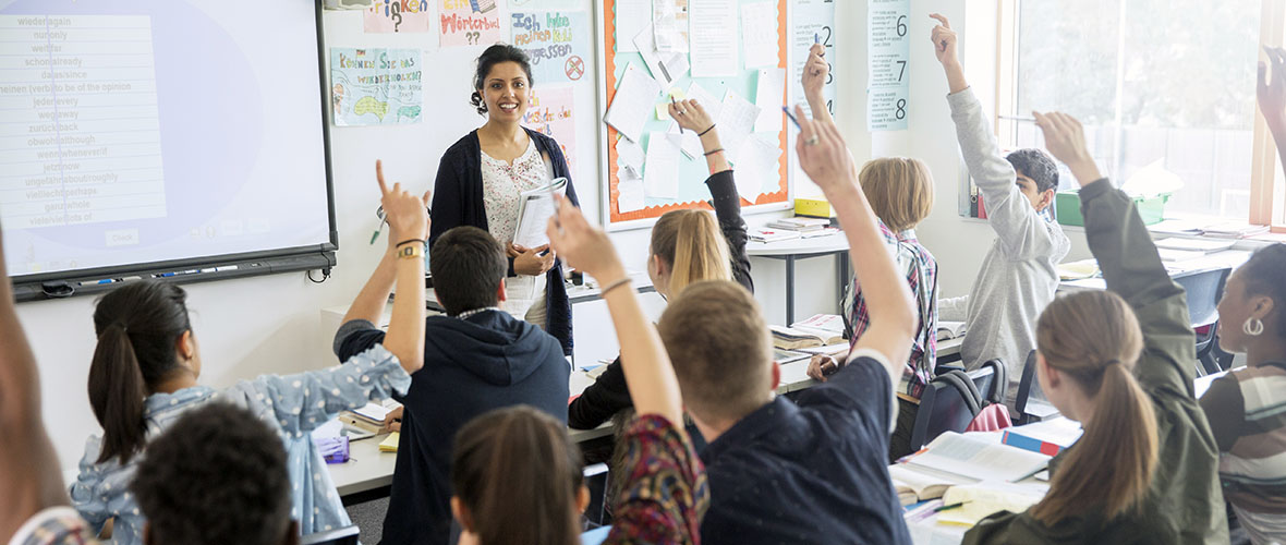 Teacher in front of class with students raising hands