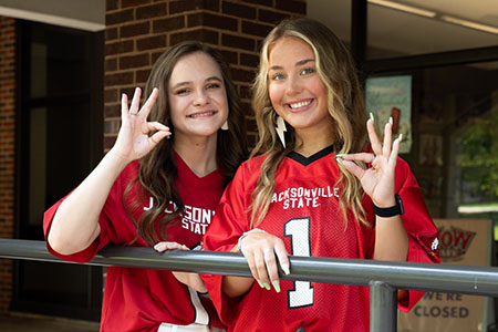 Two female students showing the Fear the Beak sign outside the dining hall