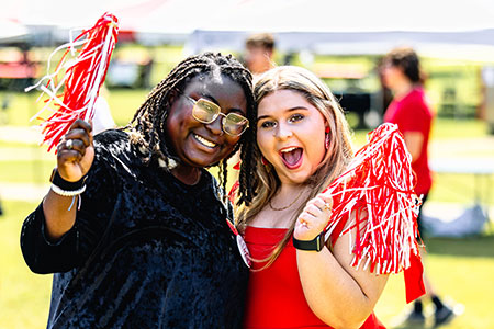 Two coeds, waving shakers on the Quad at the homecoming tailgate