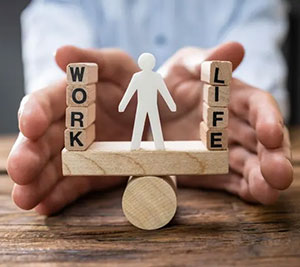 Hands cradling a wooden balancing cart with a paper doll in the center and blocks that spell out work on one side and life on the other.