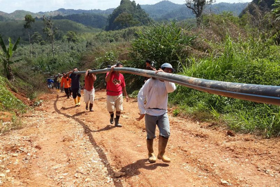 A public health worker helps carry a water line into the jungle